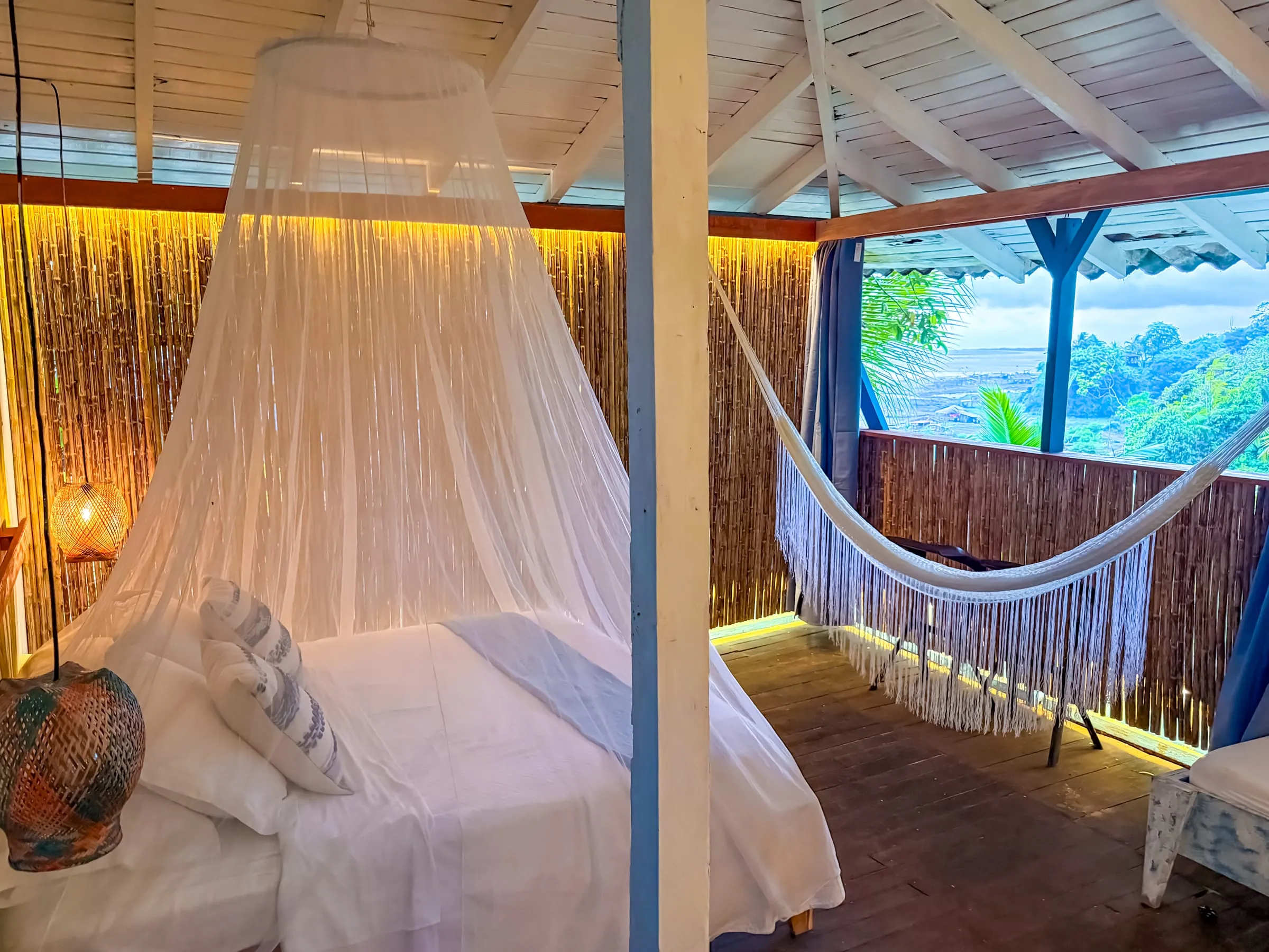Cama con mosquitero junto a la terraza de la Suite Marea, con hamaca y vista al mar