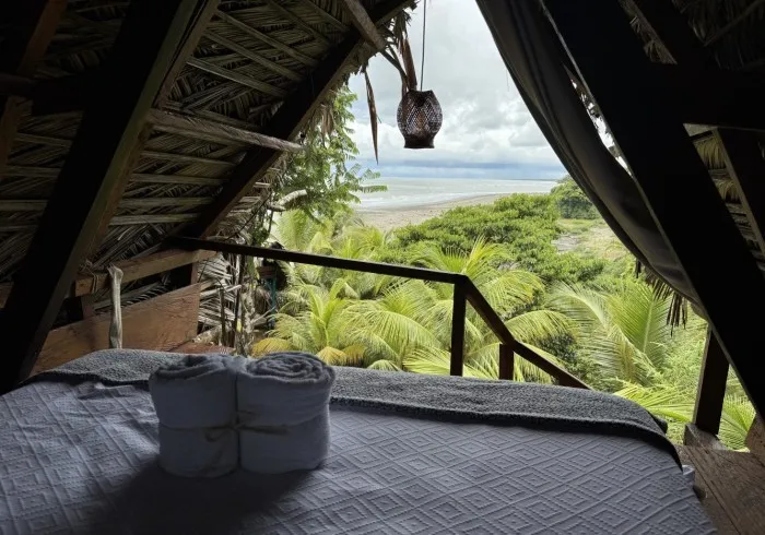 Cama de Mini 4 bajo techo de palma, con vista al mar y a la vegetación