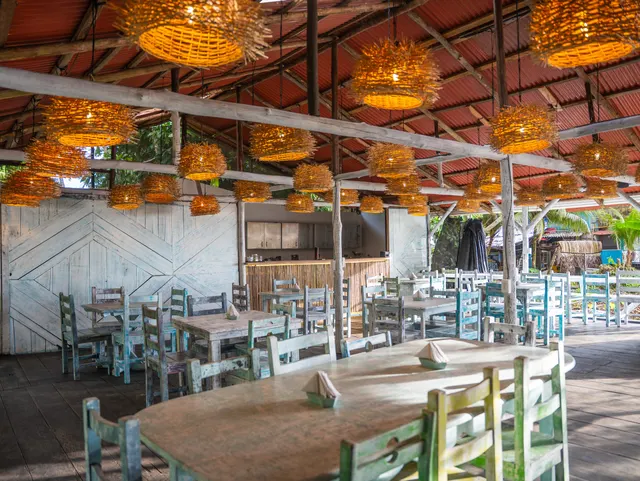 Salón del restaurante de día: mesas y sillas de madera pintadas bajo las lámparas de fibra