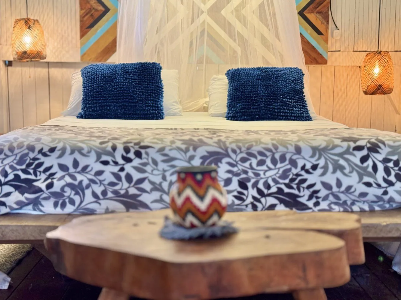 Cama con mosquitero, cojines azules y lámparas tejidas en la suite con aire acondicionado