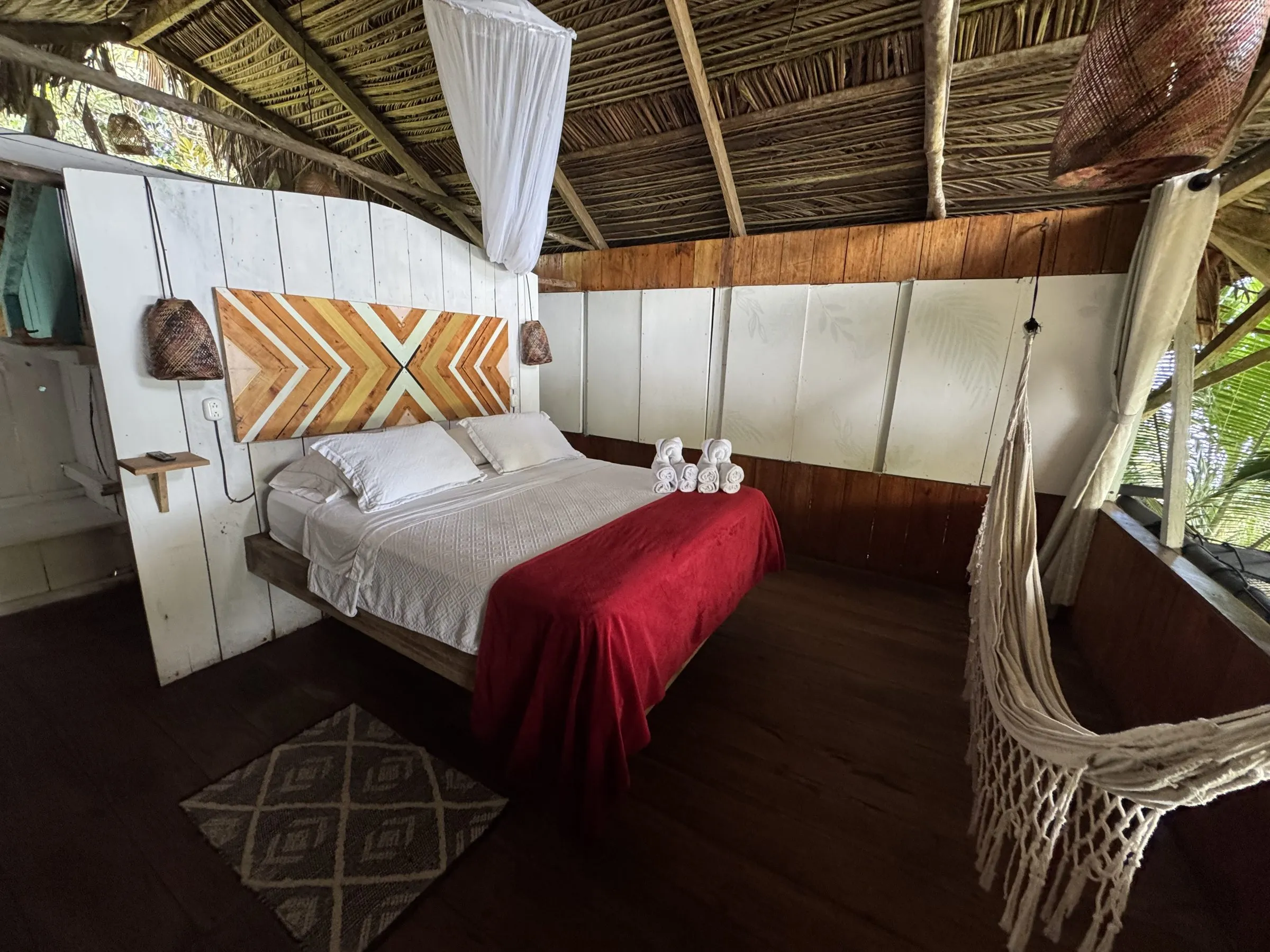 Cama de la Suite Frente Al Mar con cabecera artesanal, manta roja y hamaca junto a la ventana